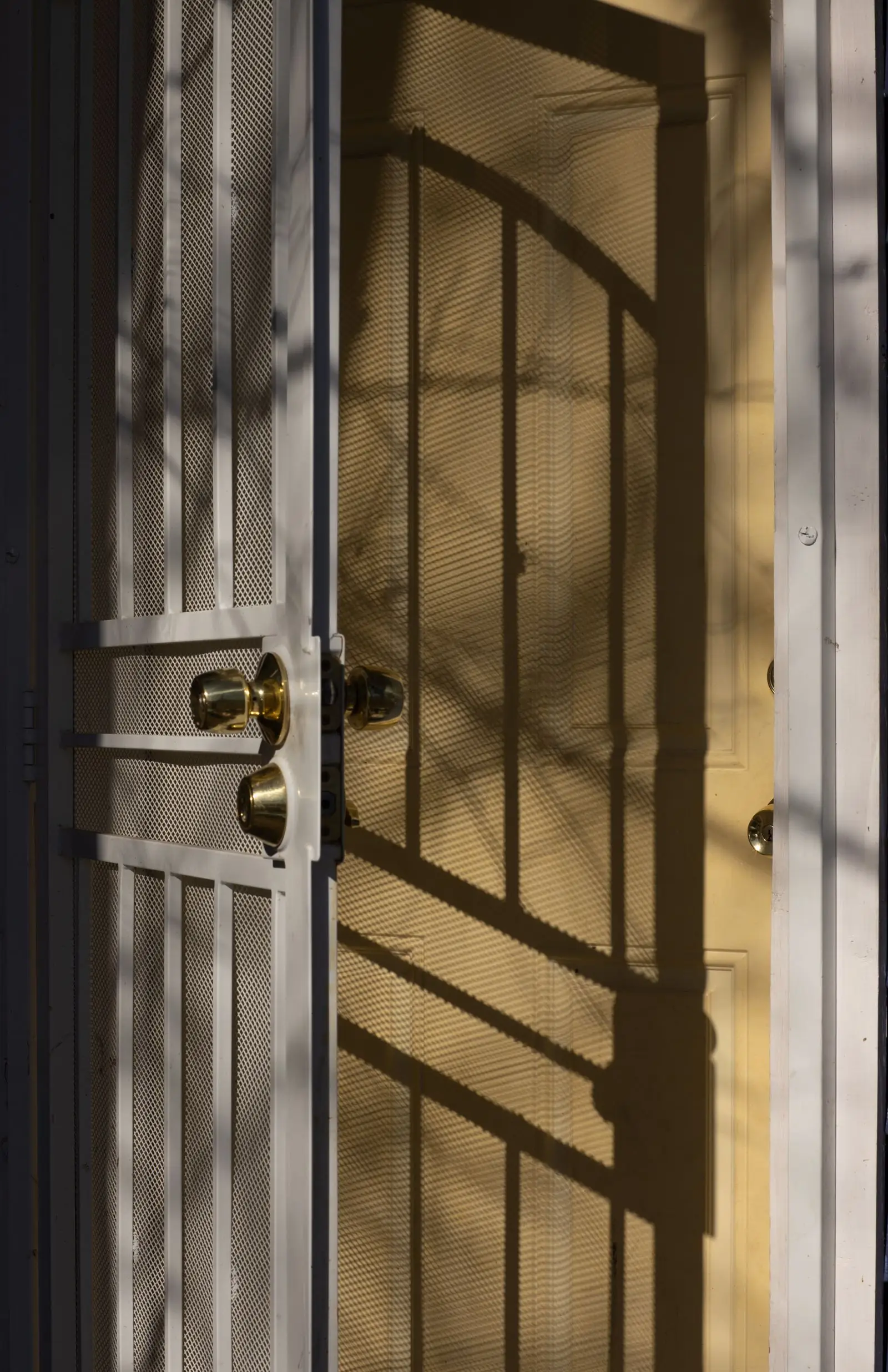 Puerta de madera con una reja metálica y pomos dorados, con la luz dibujando sombras